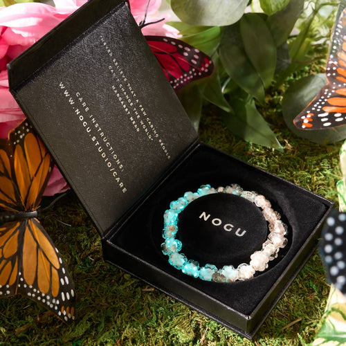Ivory Silver Firefly Glass Clover Bracelet glowing inside black NOGU gift box with butterflies and greenery